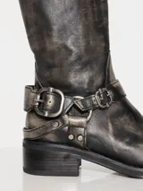 Bota de caña alta en cuero vacuno con efecto desgastado y hebillas metálicas decorativas.