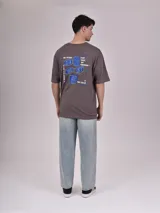 Remera blanca de corte recto con estampado de un auto clásico frente a un skyline urbano.