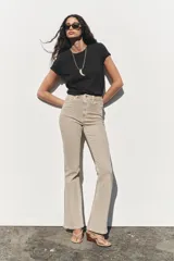 Pantalón de jean color beige, de tiro alto, corte ajustado en la cadera y muslos, y acampanado desde la rodilla. Tiene cinco bolsillos y cierre frontal con cremallera y botón.