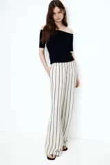 Pantalón de corte holgado en tejido liviano de mezcla de lino. Modelo de tiro alto con cintura elástica y cordón para ajustar fino, bolsillos laterales discretos y piernas rectas. Diseño a rayas verticales en blanco y negro.