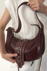 Cartera de cuero color bordó con textura croco en los laterales y tira central de napa con tachas metálicas. Incluye correa de cadena metálica entretejida en cuero, cierre superior con tirador y herrajes color níquel.