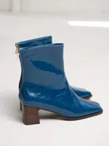 Botas de cuero charol negro con caña media y punta cuadrada. Cuentan con cierre trasero, tirador y bordado contrastante en el empeine. El taco es de madera y la suela de goma.