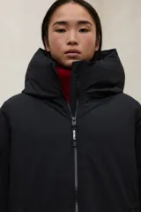 Campera acolchada larga, color blanco, con capucha grande y cierre frontal de cremallera negra. Presenta bolsillos laterales con cremallera negra.