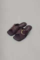 Sandalia plana de cuero, color marrón oscuro, con tira ancha cruzada sobre el empeine y hebilla metálica dorada.