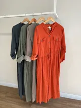 Vestido camisero largo color gris topo, de pana fina con línea italiana, cuello mao, cierre frontal con botones, mangas largas con puños abotonados, dos bolsillos de parche en el pecho, cintura ajustable con cordón y falda recta.