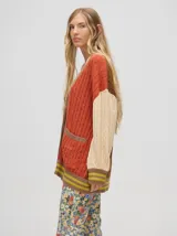 Cardigan largo color crema con detalles en color camel en el borde de los bolsillos, en el borde de los botones y en los puños. Tiene cuello en V y cierre con botones.