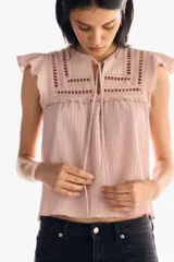 Top sin mangas color rosa pálido con textura arrugada, escote en V con tiras para atar y detalles de encaje calado en el canesú. Presenta mangas cortas con volados y corte holgado con costura fruncida bajo el busto.