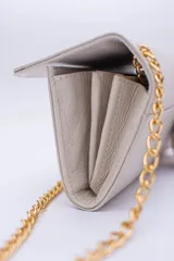 Cartera tipo sobre color beige con textura granulada y correa de cadena dorada.