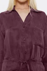 Camisa larga color borgoña, de corte recto, con cuello camisero pronunciado, manga larga con puño abotonado, cierre frontal con botones y bolsillos de fuelle en el delantero. Incluye cinturón de tela.