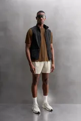 Shorts deportivos marrones de tejido técnico ligero y elástico con diferentes estructuras. Tiene forro interior, cintura elástica ajustable con cordón, bolsillos frontales, bolsillo trasero con cierre, aberturas laterales y logo estampado en la pierna.