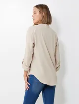 Blusa de gasa color beige, con cuello a la base y escote en V. Manga larga con presilla y botón para ajustar el largo.