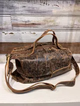 Bolso tipo bowling pequeño de cuero color chocolate con textura craquelada. Tiene doble asa corta y correa larga regulable y desmontable.