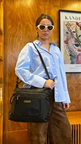 Bandolera negra de símil cuero con dos bolsillos frontales con cierre, un bolsillo trasero y tres bolsillos internos. Incluye correa larga regulable de símil cuero a tono.