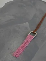 Collar con cordón de cuero marrón y dije cuadrado de metal con flecos rojos.