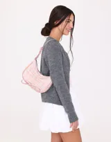 Bandolera de cuerina estampada con diseño escocés en tonos rosa y blanco. Presenta frunce y lazo frontal con moño, manija superior regulable con hebilla y cierre superior.