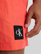 Short de baño rojo coral de largo medio, con cintura elástica y cordón ajustable. Incluye bolsillos laterales y trasero, forro de malla y logo de Calvin Klein en el lateral.