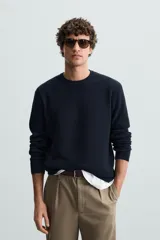 Jersey color crudo tejido en hilatura de algodón, con cuello redondo, manga larga y acabados en rib.