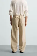 Pantalón de algodón color beige con efecto lavado, corte relajado y pierna ancha. Presenta cintura elástica con ajuste de cordón y cierre frontal con botón, además de bolsillos delanteros y bolsillos traseros de plastrón.