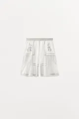 Bermuda blanca de algodón con cintura elástica, tiro alto, bordados florales, puntilla y abalorios.