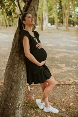 Vestido corto negro de algodón elastizado, con mangas cortas, escote redondo y falda con volados. Cuenta con una abertura sutil para facilitar la lactancia.