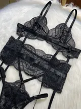 Conjunto de lencería negro de encaje, compuesto por un corpiño tipo bralette, una tanga de tira doble regulable, un portaligas desmontable y ligas regulables.