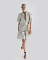 Vestido corto color blanco con estampado de lunares negros, escote en V, mangas cortas abullonadas y falda con volantes.