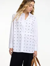 Camisa blanca de algodón con cuello camisero, cierre frontal con botones y tachas plateadas en el frente.