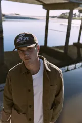 Gorra marrón de cinco paneles con bordado frontal con la inscripción "TT Archive Club Creative Dept. Established 1990".