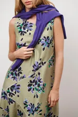 Vestido midi color beige con estampado de hojas en tonos violeta, verde y negro. Diseño sin mangas, con escote redondo y falda acampanada.