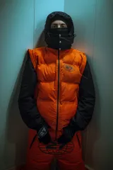 Campera puffer naranja con capucha desmontable y mangas desmontables, con logo reflectivo en el pecho.