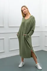 Vestido largo de tejido acanalado color verde oliva, con capucha, escote en V y mangas largas. Presenta bolsillos laterales y aberturas en los bajos.
