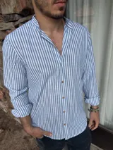 Camisa de manga larga con cuello mao a rayas verticales celestes y blancas, con botones de madera. Las mangas pueden arremangarse.