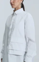 Camisa blanca de manga larga, confeccionada en poplín de algodón, con calce oversize y un bolsillo frontal asimétrico y poco convencional.
