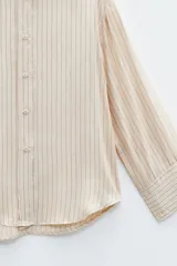 Camisa color crema con rayas verticales finas, de corte holgado y más larga en la parte posterior.