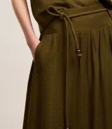 Pollera evasê midi color verde militar, confeccionada en crepé con cintura ancha con trabillas en los laterales y elástico detrás de la cintura. Incluye cinturón de cuerda para lazo con abalorios de puntas.