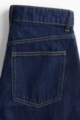 Pantalón de jean azul oscuro de tiro alto, corte recto y pierna ancha. Diseño de cinco bolsillos con costuras a la vista. Inspirado en los años 70.