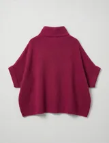 Capa o poncho tejido color verde esmeralda, con cuello polera alto que se cierra con un botón grande en el lateral. Presenta mangas cortas estilo japonesa y un calce amplio.