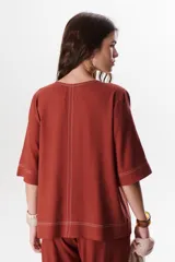 Blusa de lino color beige claro, con mangas 3/4 y cuello redondo. Presenta pespuntes a contratono en el centro, puños y ruedo.