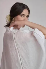 Camisa blanca de lino con cuello clásico, cierre frontal con botones y mangas anchas 3/4. Presenta detalles de bordado calado en el frente y puños.