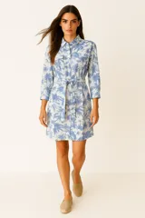 Vestido camisero corto con estampado de palmeras en tonos celeste y blanco, con cuello camisero, abotonadura frontal, mangas 3/4 y cinturón de lazo.