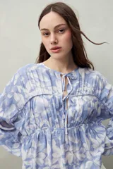 Blusa estampada celeste y blanca de caída fluida con cuello redondo y lazos frontales. Diseño con cortes horizontales y frunces, mangas largas con puños elastizados.