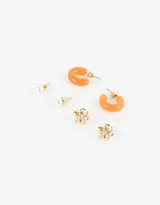 Set de tres pares de aros: un par de aros pasantes con perlas, un par de aros pasantes con forma de flor dorada y un par de aros argolla de resina translúcida color naranja.