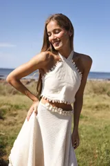 Top halter de lino color crudo, con escote enmarcado por bordes festoneados y tiras cruzadas en la espalda.