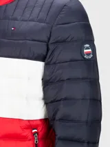 Chaqueta acolchada Tommy Hilfiger con diseño a bloques de color azul marino, blanco y rojo. Tiene cuello alto, cierre de cremallera, dos bolsillos delanteros con cremallera y logo bordado en el pecho.