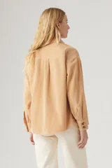 Camisa color beige de pana con corte recto, cuello camisero, cierre con botones a tono, dos bolsillos frontales con solapa abotonada y mangas largas con puños abotonados.