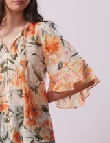 Blusa de gasa estampada con flores color naranja, marca Figueroa & Flower. Tiene cuello a la base, escote en V con lazo, abertura central con botones, delantera plisada y mangas 3/4 amplias.