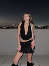 Conjunto de top halter y minifalda, ambos de lentejuelas negras. El top es corto y tiene un escote pronunciado. La falda es ajustada y de tiro alto.