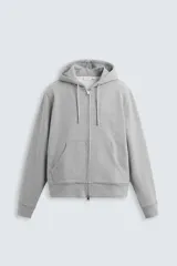 Sudadera negra relaxed fit confeccionada en tejido de algodón compacto con interior en rizo. Cuello con capucha ajustable y manga larga. Bolsillos frontales tipo canguro. Acabados en rib. Cierre frontal con cremallera.