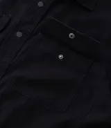 Camisa de manga larga color marrón, confeccionada en sarga de algodón, con cuello inglés, botones frontales y dos bolsillos de parche con solapa y botón en el pecho.