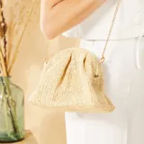 Bolso bandolera color beige, tejido en rafia con patrón de espiga. Tiene forma rectangular con cierre superior fruncido y cadena dorada para colgar al hombro.